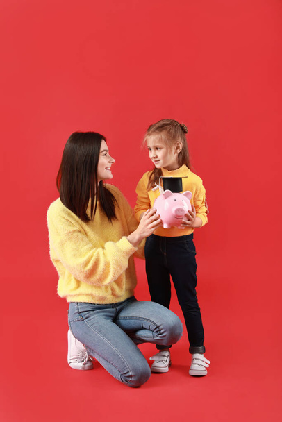 Little girl and her mother with savings for education on color background - Valokuva, kuva