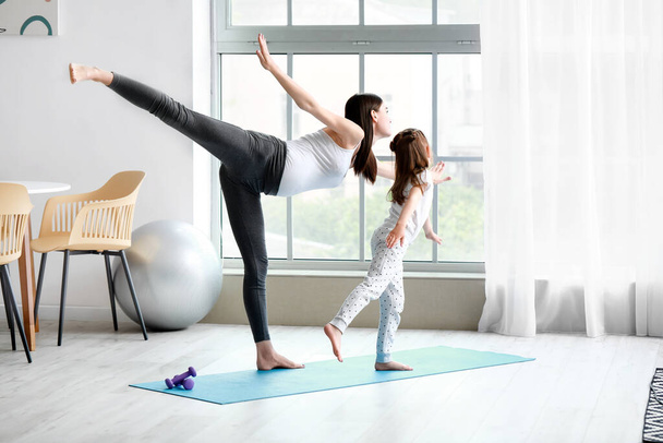 Young pregnant woman and her little daughter practicing yoga at home - Photo, Image