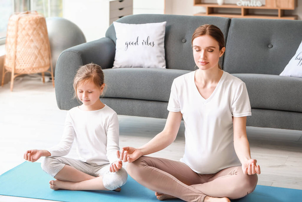 Junge schwangere Frau und ihre kleine Tochter praktizieren Yoga zu Hause - Foto, Bild