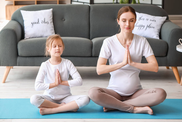 Young pregnant woman and her little daughter practicing yoga at home - Photo, image