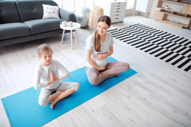 Młoda ciężarna kobieta i jej córeczka ćwiczą jogę w domu - Zdjęcie, obraz