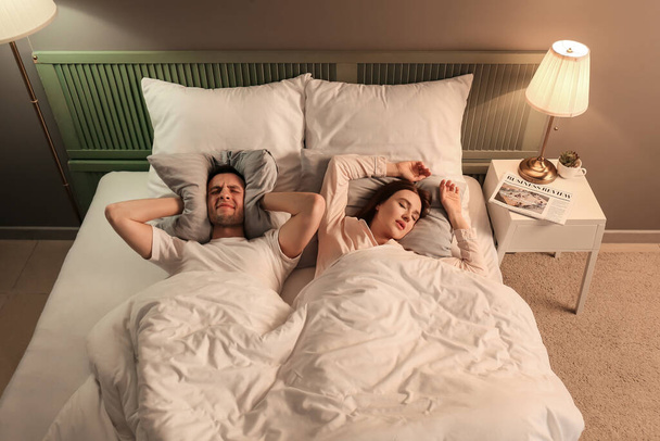 Junger irritierter Mann im Bett mit schnarchender Frau - Foto, Bild