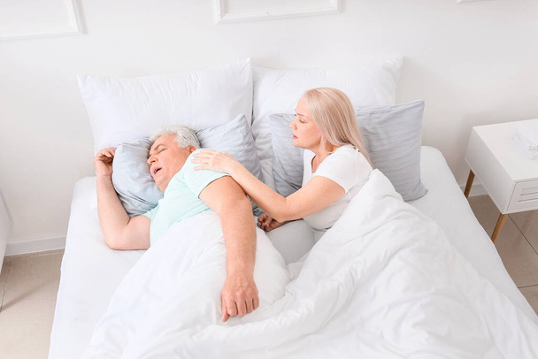 Зрелая раздраженная женщина в постели с храпящим мужем - Фото, изображение