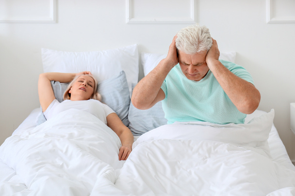 Mature irritated man in bed with snoring wife - Foto, afbeelding