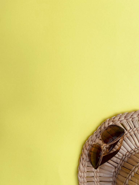 Heller Sommer-Strohhut und dunkle Sonnenbrille auf gelbem Hintergrund - Foto, Bild