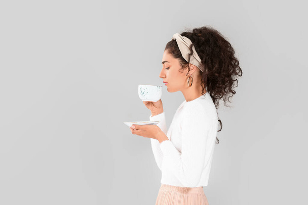 Hermosa joven con té caliente sobre fondo gris
 - Foto, Imagen