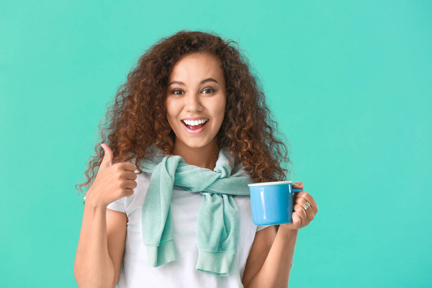 Beautiful young African-American woman with hot tea showing thumb-up on color background - Φωτογραφία, εικόνα