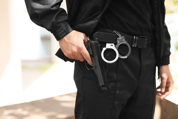 Male police officer with gun outdoors, closeup - 写真・画像