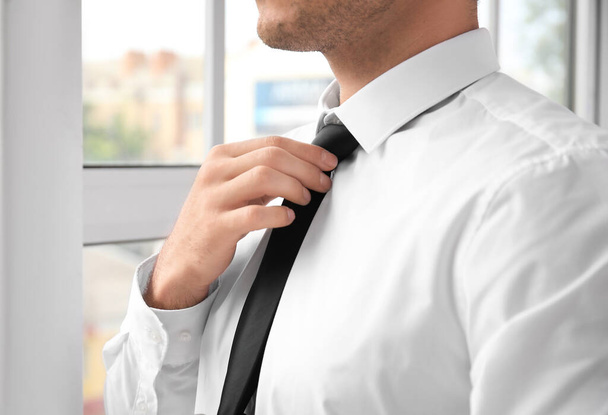 Νεαρός επιχειρηματίας με κομψό πουκάμισο κοντά στο παράθυρο στο γραφείο, κοντινό πλάνο - Φωτογραφία, εικόνα