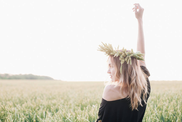 Young, slender girl in a wreath of wheat ears at sunset in a field - Photo, image
