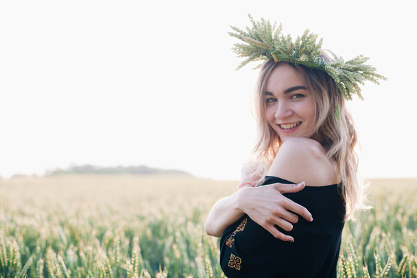 Young, slender girl in a wreath of wheat ears at sunset in a field - Photo, Image