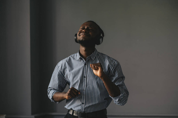 Young african man listening to music with wireless earphones and dancing at home - Foto, Bild