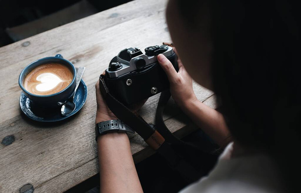 Asyalı bir kadın kahve dükkanında oturmuş film kamerasıyla fotoğraf çekiyor. - Fotoğraf, Görsel