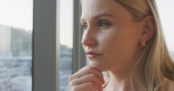 Close up of a thoughtful Caucasian professional businesswoman working in a modern office looking out of a window at a stunning view of a city in slow motion. - Materiaali, video