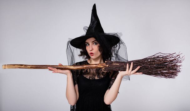 portré a meglepett fiatal szép nő fekete boszorkány halloween jelmez seprű felett fehér háttér - Fotó, kép