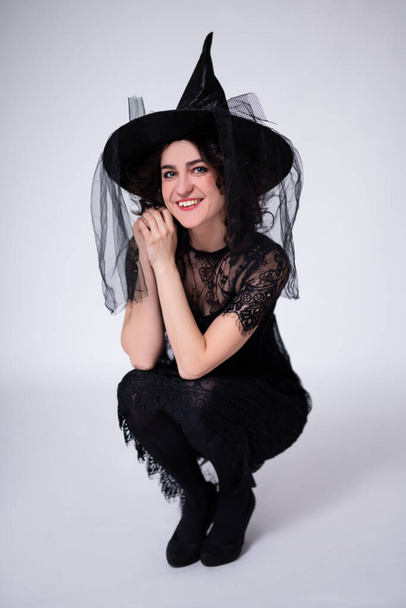 mosolygós nő fekete boszorkány halloween jelmez és kalap pózol fehér háttér - Fotó, kép