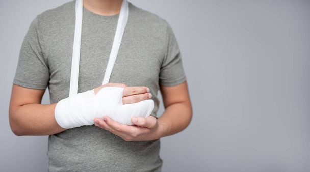 first aid concept - young man with bandage and gypsum on his broken hand and copy space over gray - Photo, image