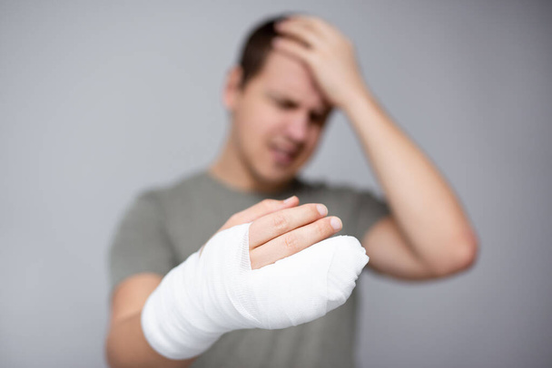 injury and first aid concept - unhappy man with broken hand in bandage and gypsum - 写真・画像