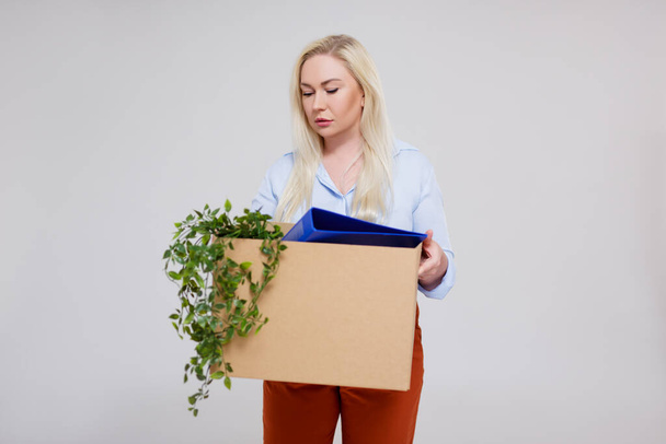 mujer de negocios infeliz sosteniendo caja de cartón de pertenencias después de ser despedida de su trabajo, copiar espacio sobre fondo gris
 - Foto, Imagen