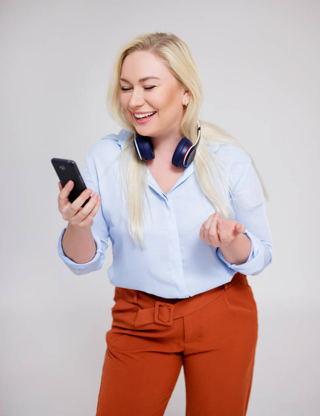 portré boldog szép plusz méret szőke nő hallgat zenét, és használja okos telefon szürke háttér - Fotó, kép