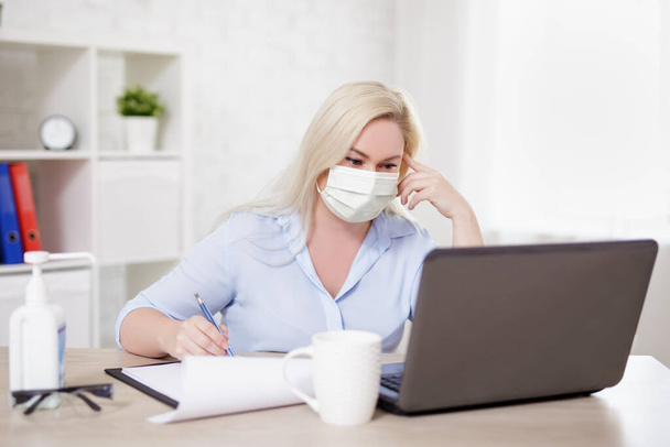 бизнес, здравоохранение, безопасность и пандемическое понятие коронавируса - блондинка в маске, работающая с ноутбуком дома или в офисе
 - Фото, изображение