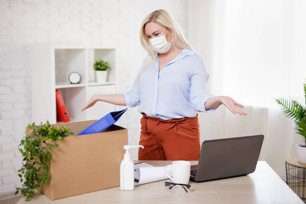 business, financial crisis, health care, safety and corona virus pandemic concept - woman in mask packing belongings after getting fired from her work - Фото, изображение