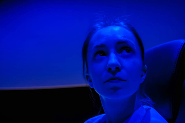Γυναίκα πρόσωπο κοιτάζοντας γύρω στο σινεμά με μπλε φως φωτισμού - Φωτογραφία, εικόνα