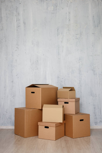 concepto de día móvil - cajas de cartón marrón con pertenencias apiladas en el suelo y espacio de copia sobre fondo de pared gris
 - Foto, Imagen