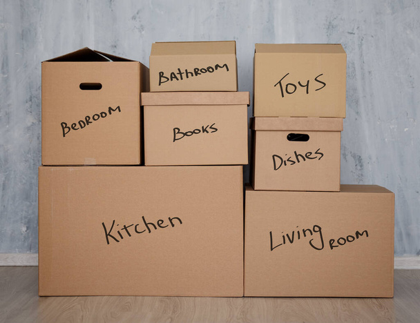 moving day concept - stack of brown cardboard boxes with domestic things over gray wall background - Photo, Image