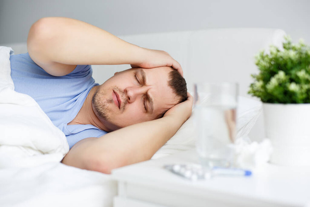 egészségügyi ellátás és betegség koncepció - portré beteg ember láz vagy fejfájás feküdt az ágyon otthon vagy kórházban - Fotó, kép