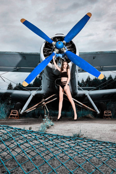 young beautiful girl in a black swimsuit stands at the propeller of the plane in a headset - Photo, Image