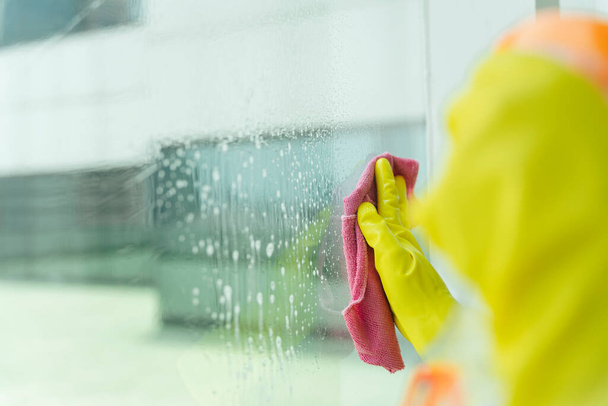 Schoonmaakster hand dragen gele handschoenen schoonmaken spiegel met roze doek. Covid-19 Coronaviruspreventie. - Foto, afbeelding