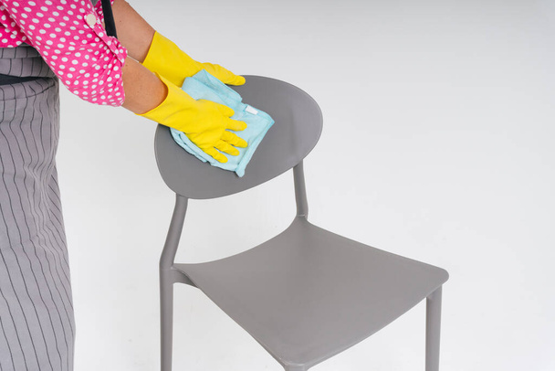 Cleaner woman wearing protective yellow gloves cleaning chair furniture. Covid-19 Coronavirus prevention. - Photo, Image