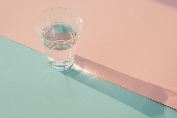 Призма тени стеклянной чашки воды на пастельно-голубом и розовом фоне
. - Фото, изображение