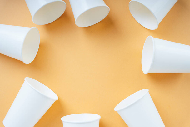 Одноразові паперові чашки розташовані візерунком на помаранчевому фоні. Перероблені паперові стаканчики
. - Фото, зображення