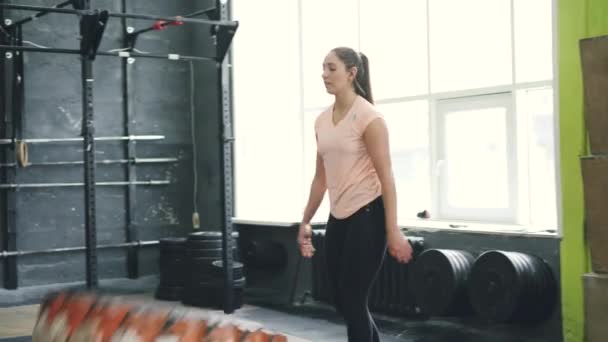 Young fit sportswoman lifting heavy rubber tyre during crossfit workout indoors - Video, Çekim