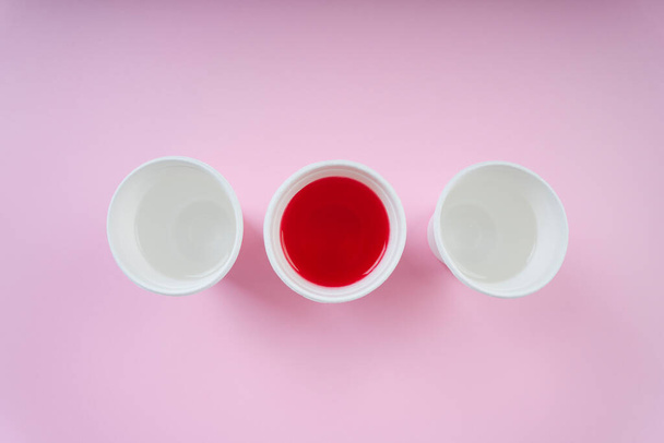 トップビュー-ピンクの背景に2つのウォーターカップと1つの赤い輝くソーダ. - 写真・画像