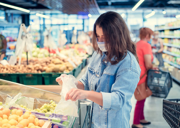Hermosa chica en una máscara en su cara en un supermercado hace compras
 - Foto, Imagen