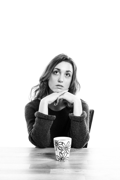 νεαρή γυναίκα που κάθεται στο τραπέζι με ένα φλιτζάνι καφέ κοιτώντας ψηλά. - Φωτογραφία, εικόνα