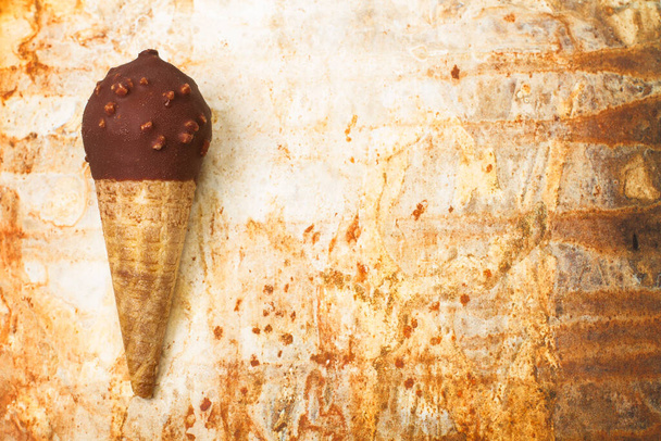 Čokoládová zmrzlina kornout s arašídy lupínky na zrezivělém kovovém stole s kopírovacím prostorem - Fotografie, Obrázek