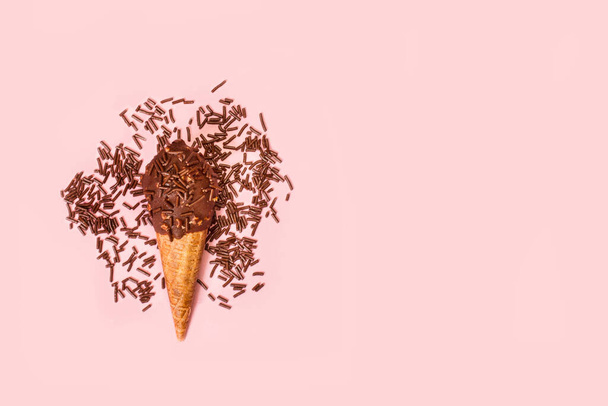 Chocolate ice cream cone with chocolate sprinkles on a pink background with copy space - Fotó, kép