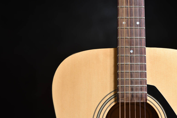 Acoustic light wood guitar with metal strings close-up against a dark background and copy space - Foto, imagen