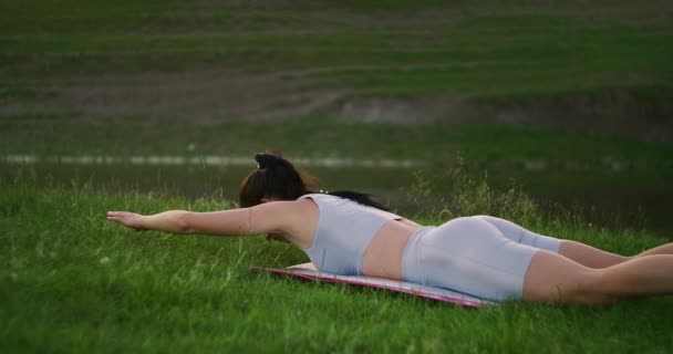 Ξαπλωμένη στο χαλάκι, η γυναίκα σηκώνει το σώμα πάνω από το έδαφος και απλώνει τα χέρια της στις πλευρές κάνοντας ασκήσεις για τους μυς της πλάτης. - Πλάνα, βίντεο