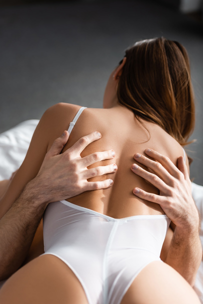 Back view of man embracing sexy woman in white bodysuit on bed - Foto, Imagen