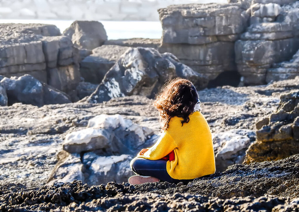 Femme en chemisier jaune assise sur un rocher regardant une paroi rocheuse - Photo, image