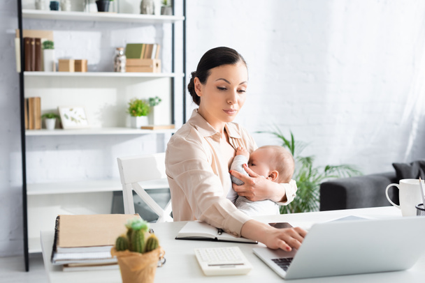 selective focus of mother breastfeeding infant son while using laptop at home - Photo, Image