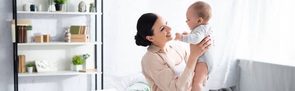 panoramic shot of cheerful mother holding in arms cute infant son in baby romper  - Фото, зображення