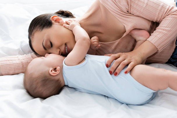 mother with closed eyes lying on bed with baby boy  - Valokuva, kuva