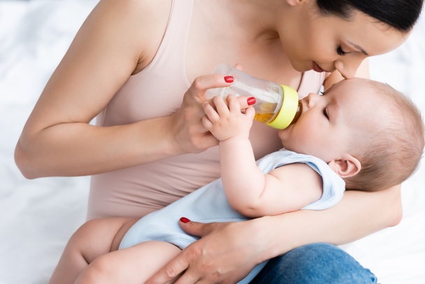 mother feeding cute infant son while holding baby bottle - Photo, Image