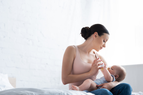 красива жінка годує милого немовляти сина, тримаючи пляшку для немовлят
 - Фото, зображення